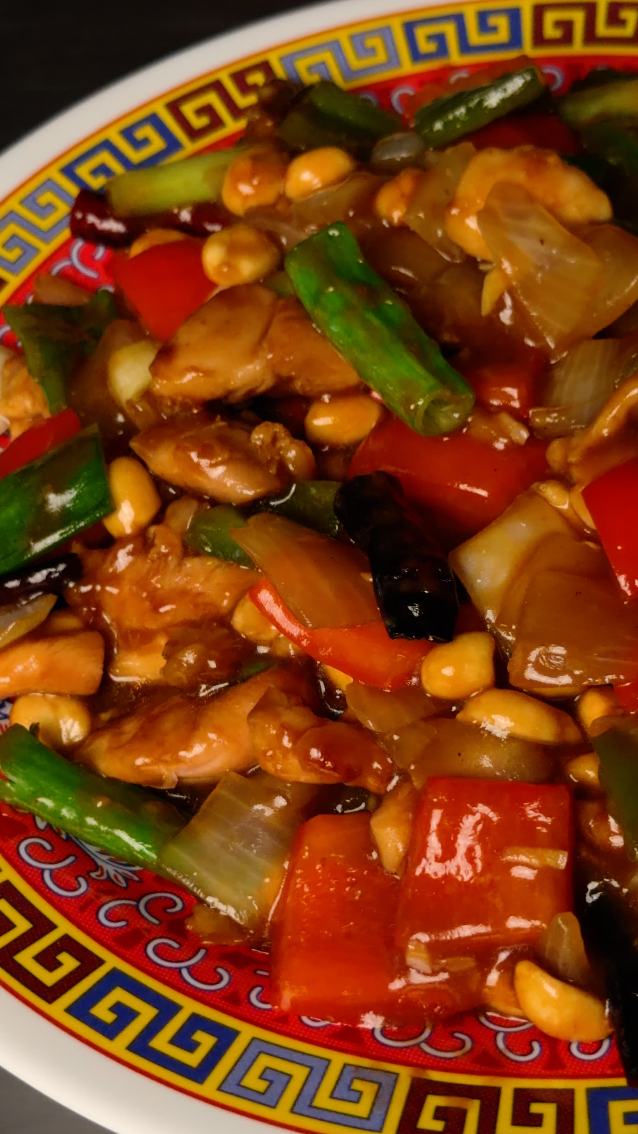 Takeout-style Kung Pao chicken with red and green peppers, dried chilies, and roasted peanuts on a Chinese-pattern plate